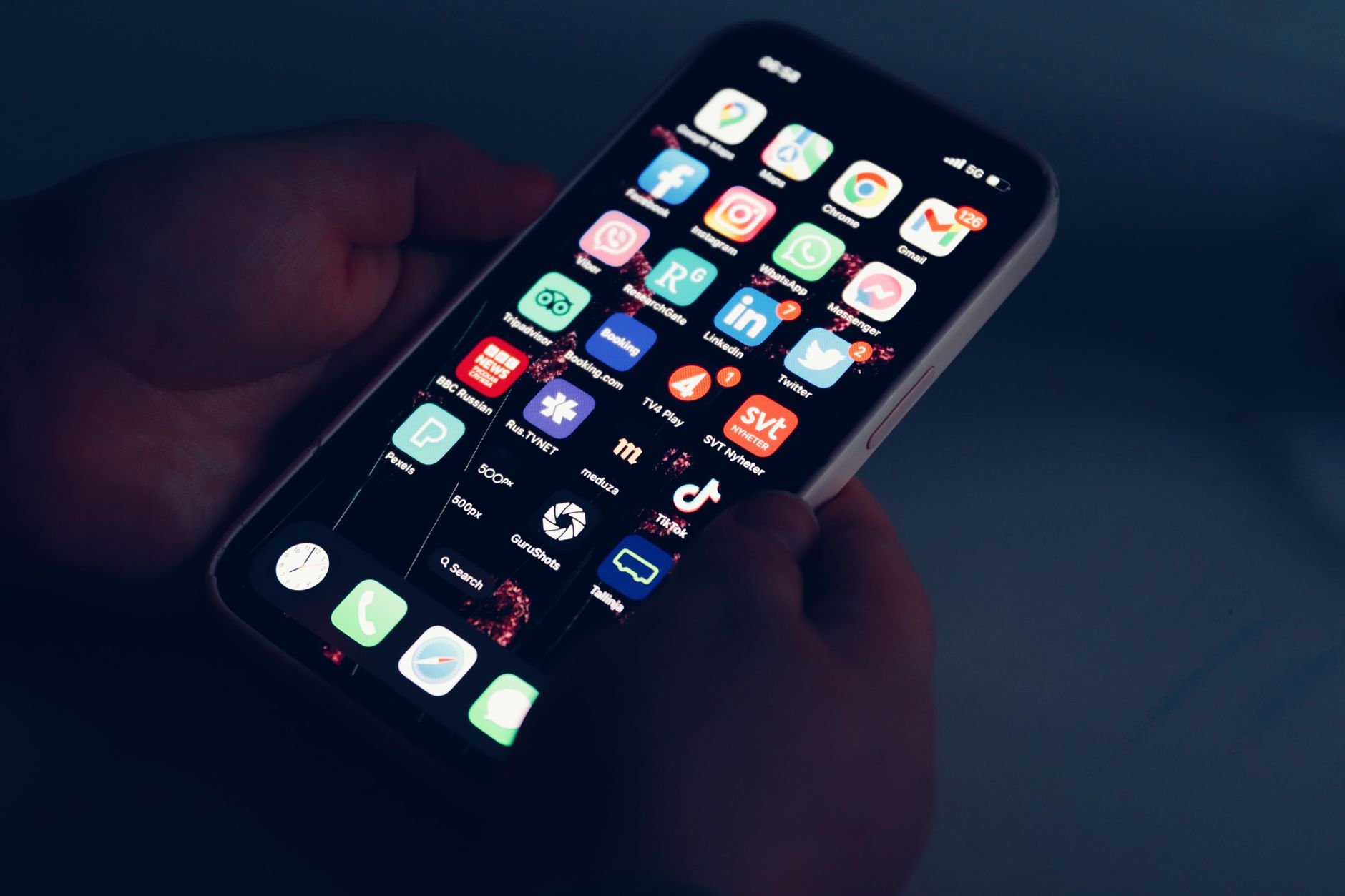Hand holding smartphone with dark home screen displaying colorful app icons including social media and entertainment applications