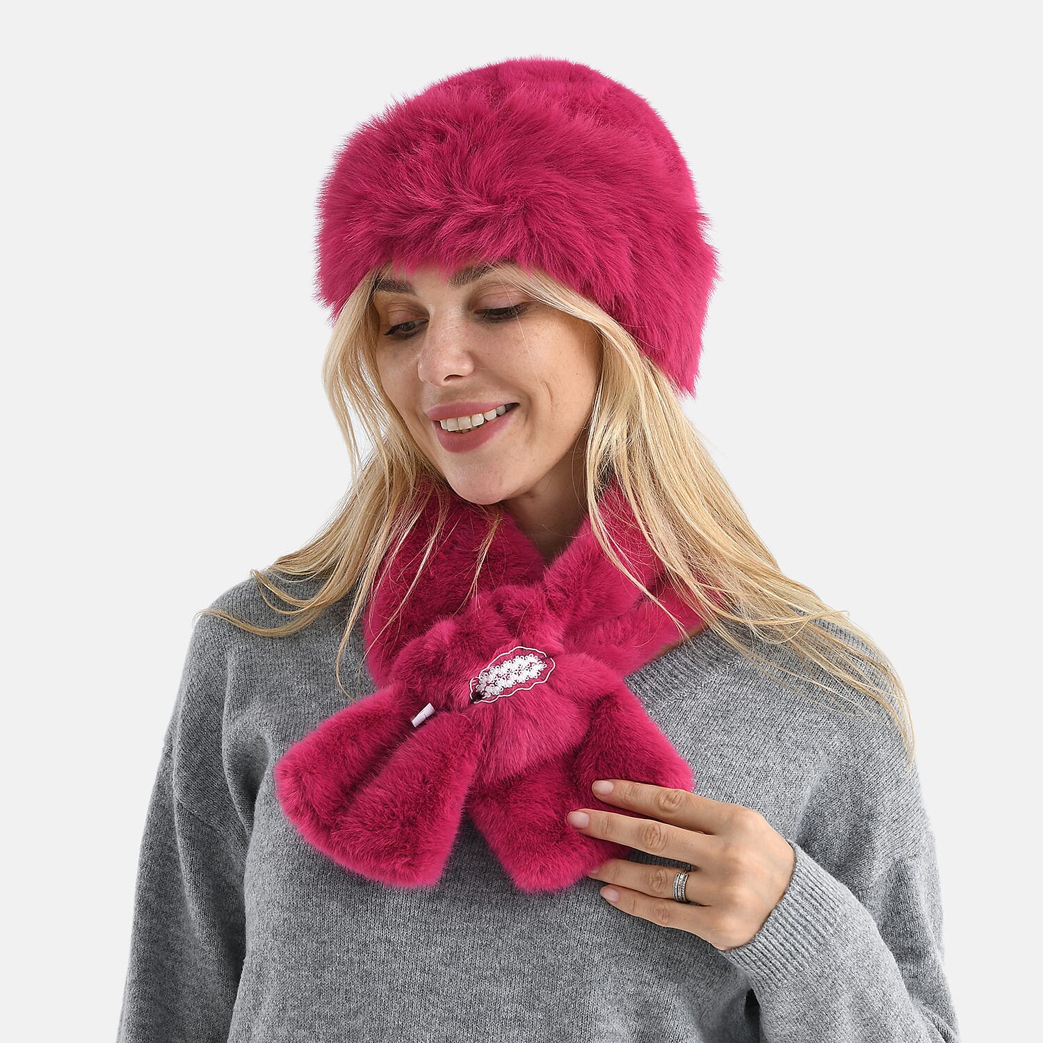Woman in gray sweater wearing hot pink faux fur hat and matching scarf, smiling while looking down