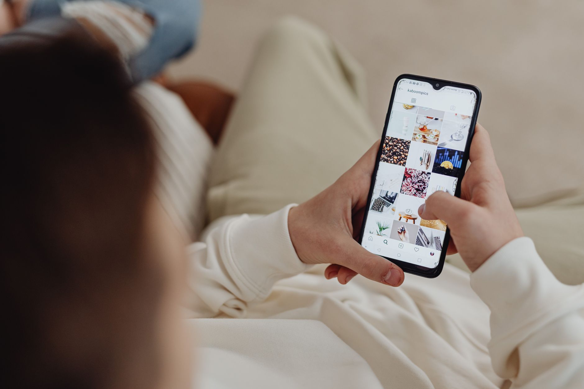 Person in cream-colored clothing viewing smartphone displaying grid of food photography and aesthetic lifestyle images
