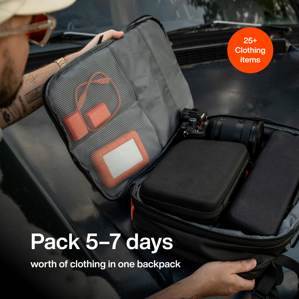 Open black backpack showing mesh compartments with orange accents containing camera gear and clothing items