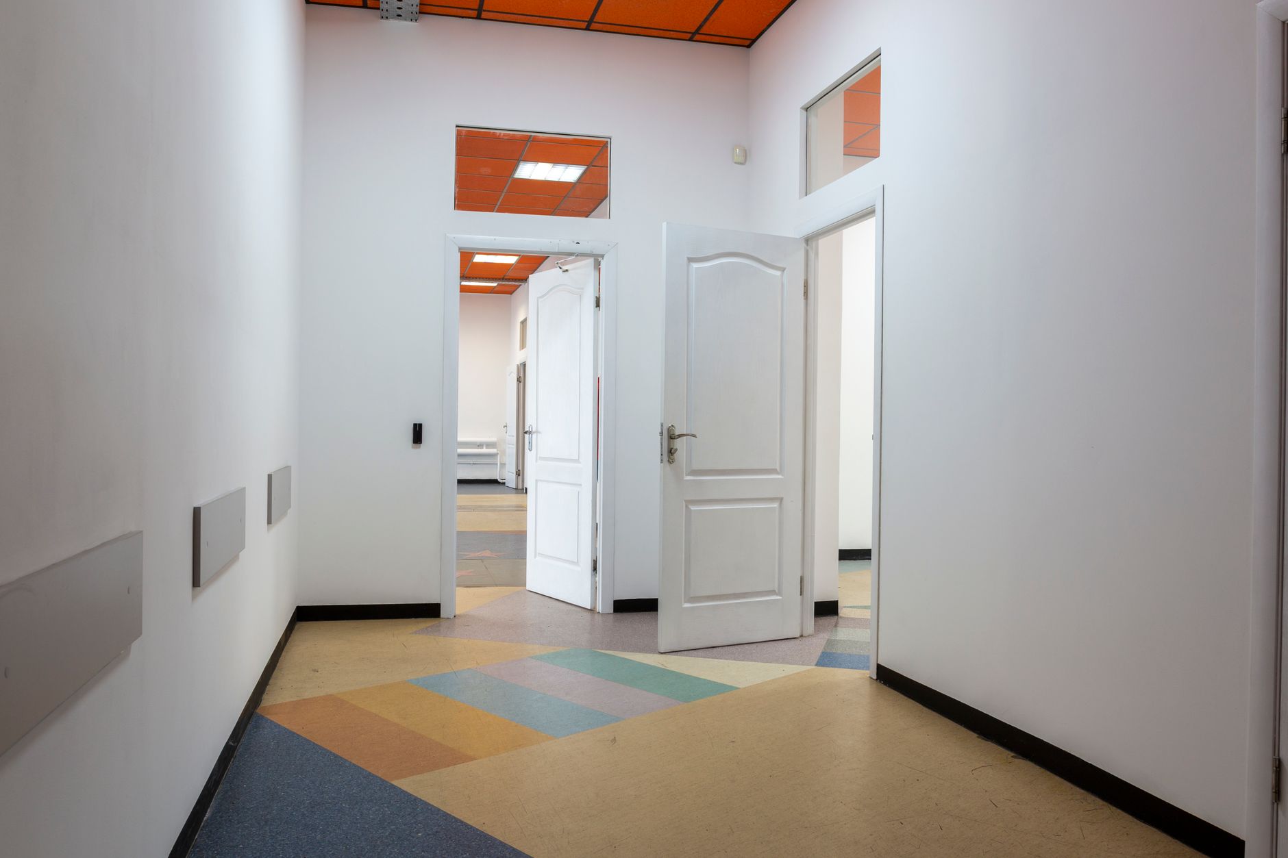 Empty hallway with white doors, orange ceiling panels, and colorful geometric floor mat design