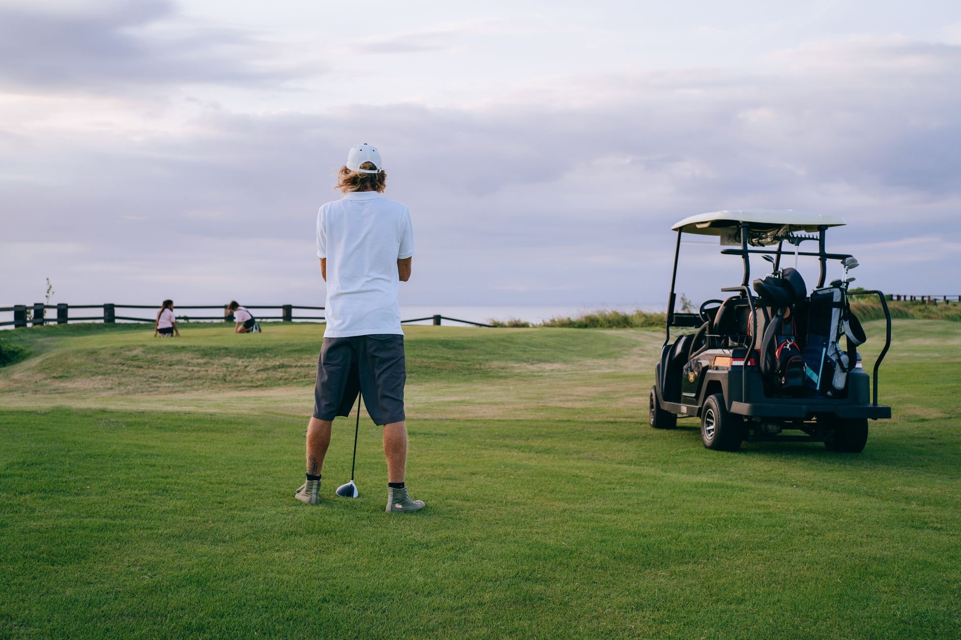 Golfer standing on fairway preparing to hit ball with golf cart in background