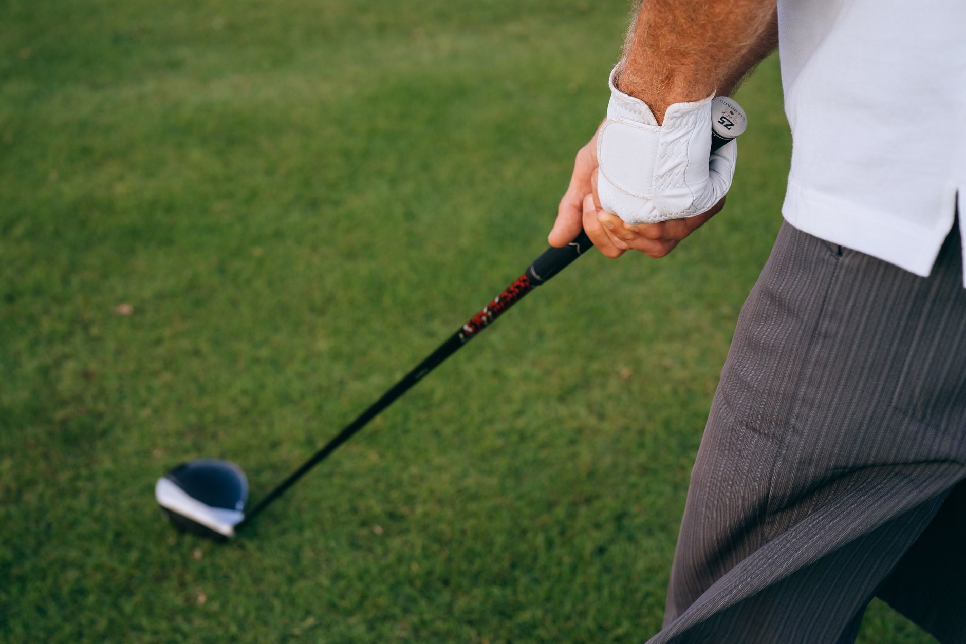 Golfer's hands holding a driver with white golf glove on a putting green