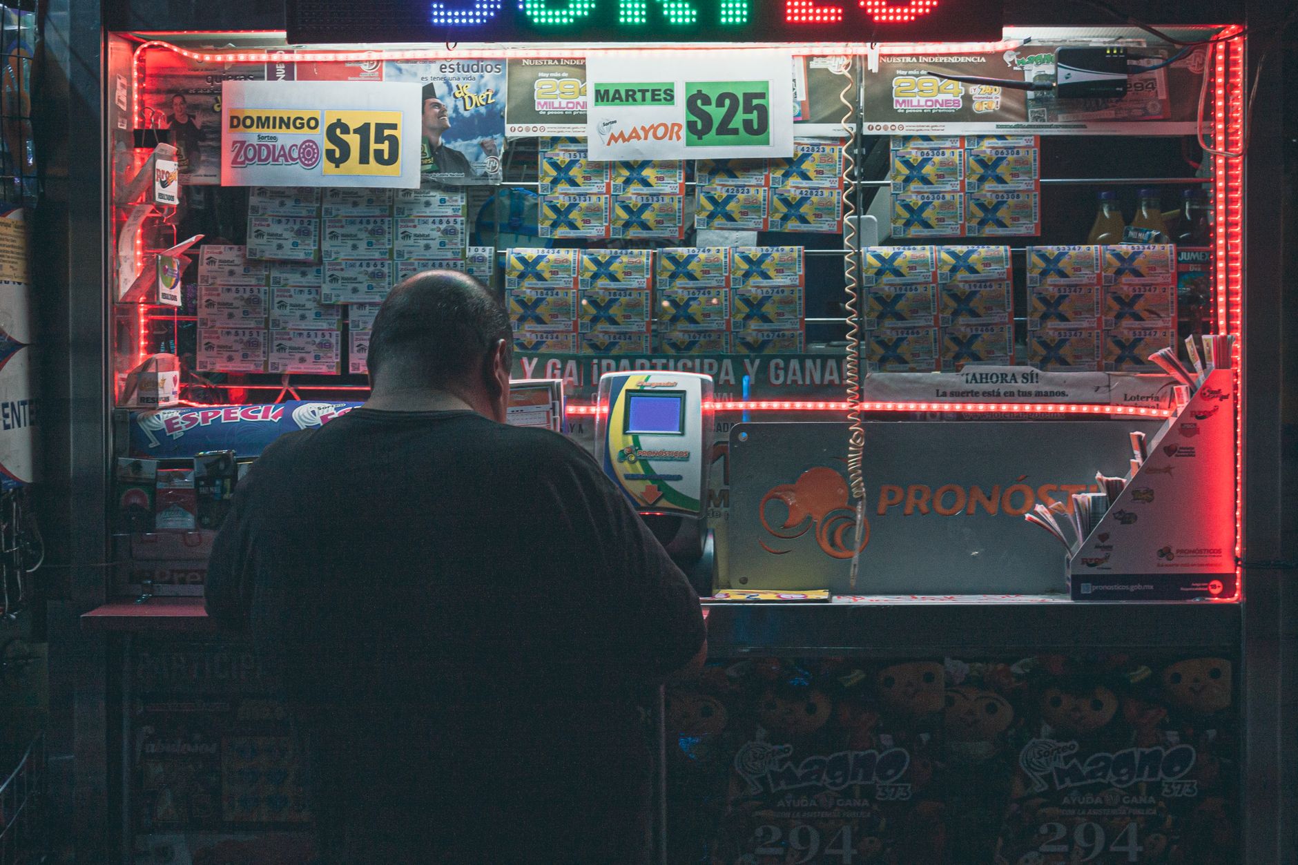 Homme de dos devant un écran de jeux de loterie avec des affiches de prix et des néons rouges
