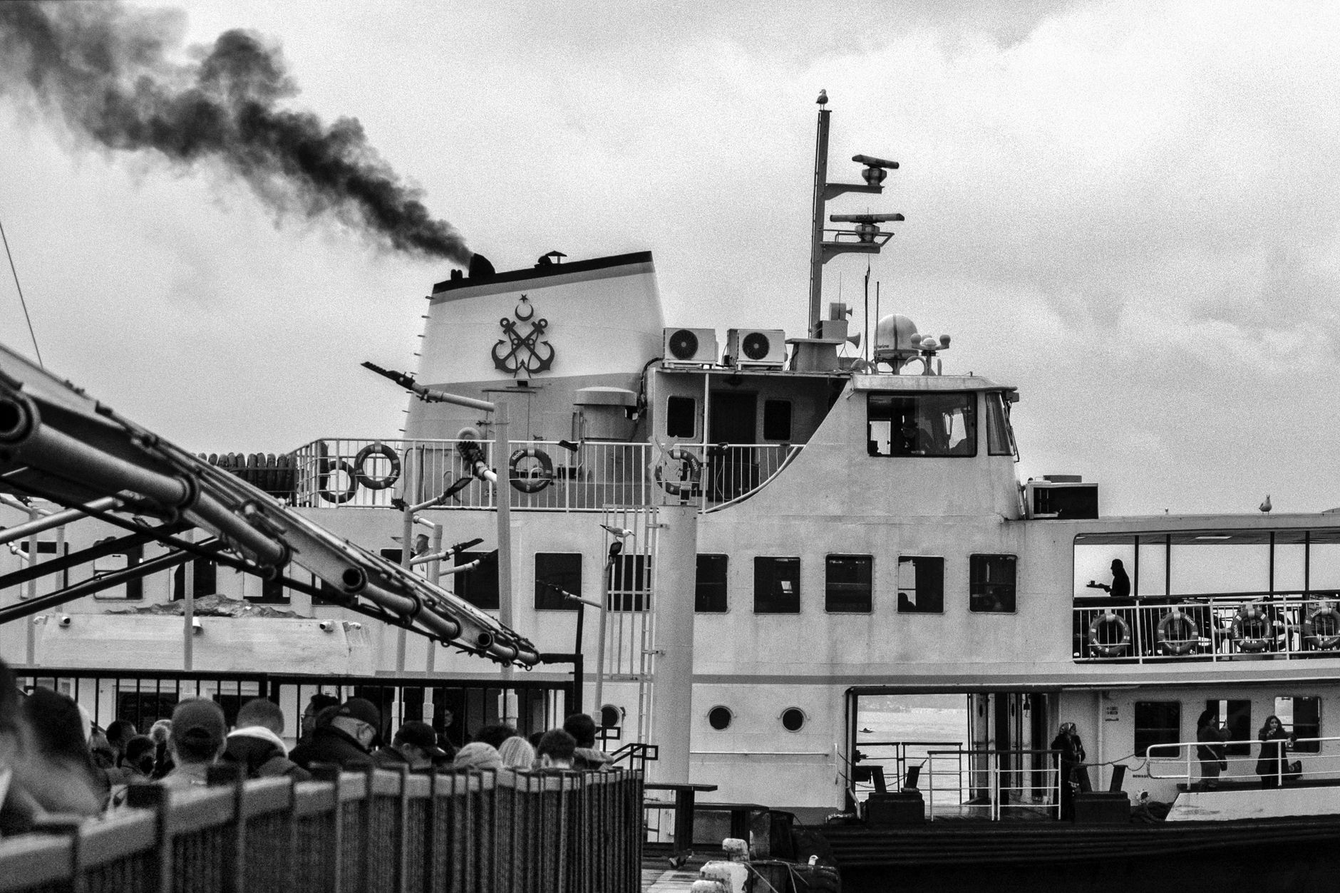 Historische Schwarzweiß-Aufnahme einer Passagierfähre mit Rauchwolken aus dem Schornstein und Passagieren an Deck.