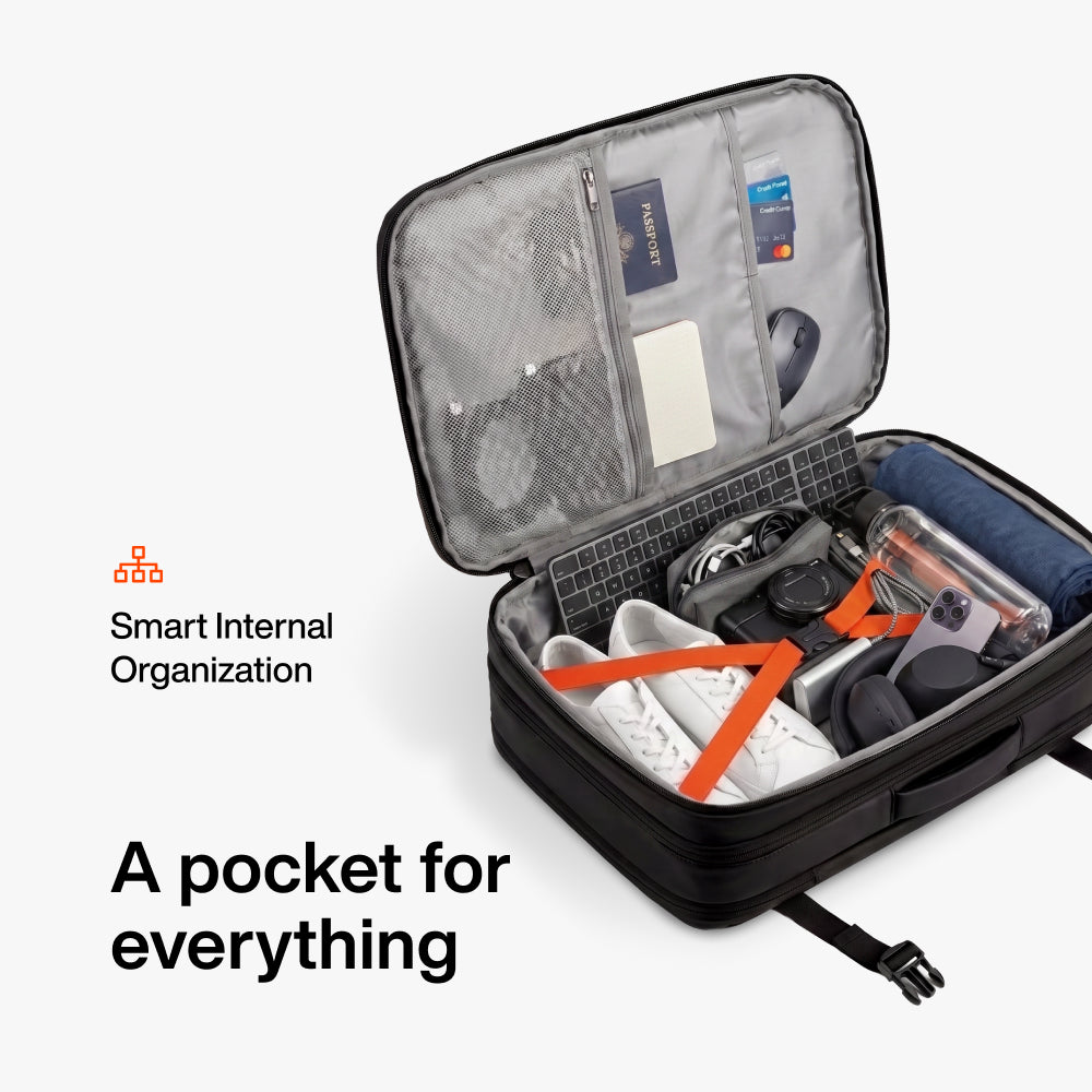 Open black packing cube with organized compartments containing white shoes, electronics, keyboard, and travel documents