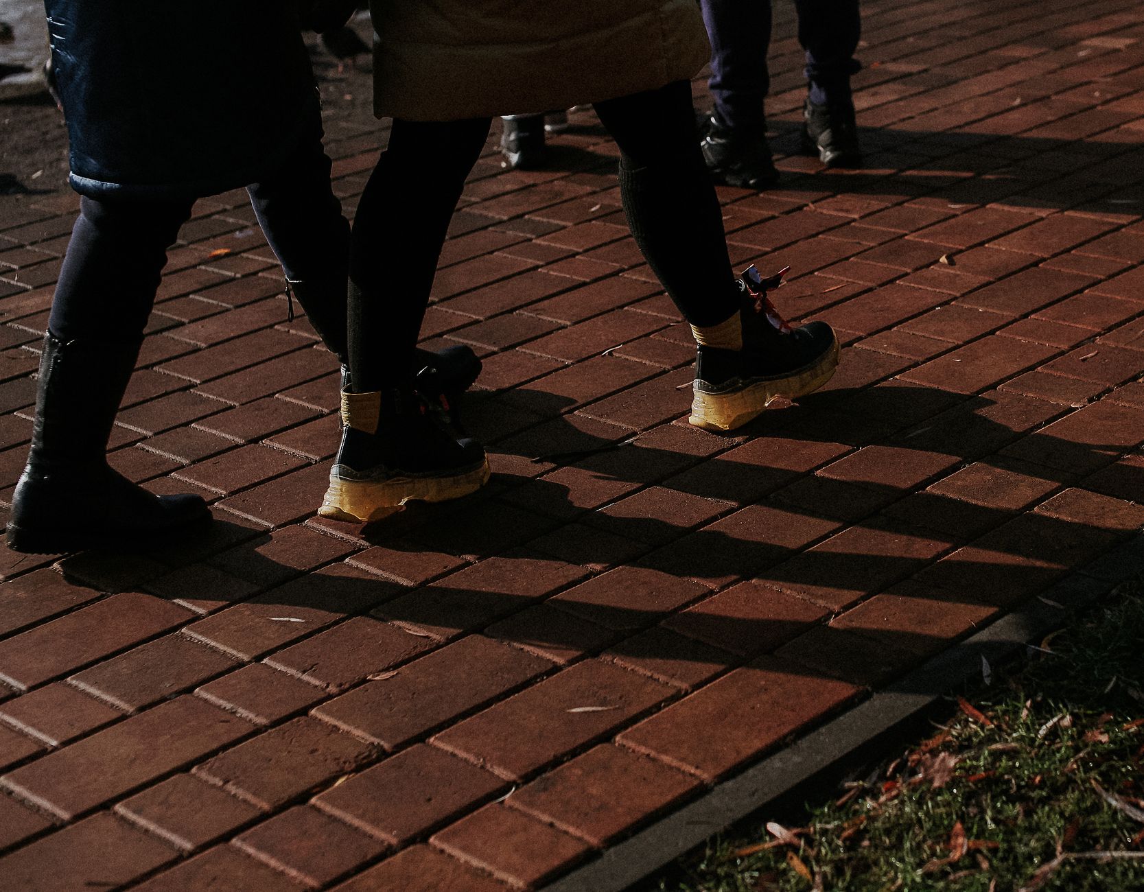 People wearing black boots with tan rubber heels standing on red brick pavement