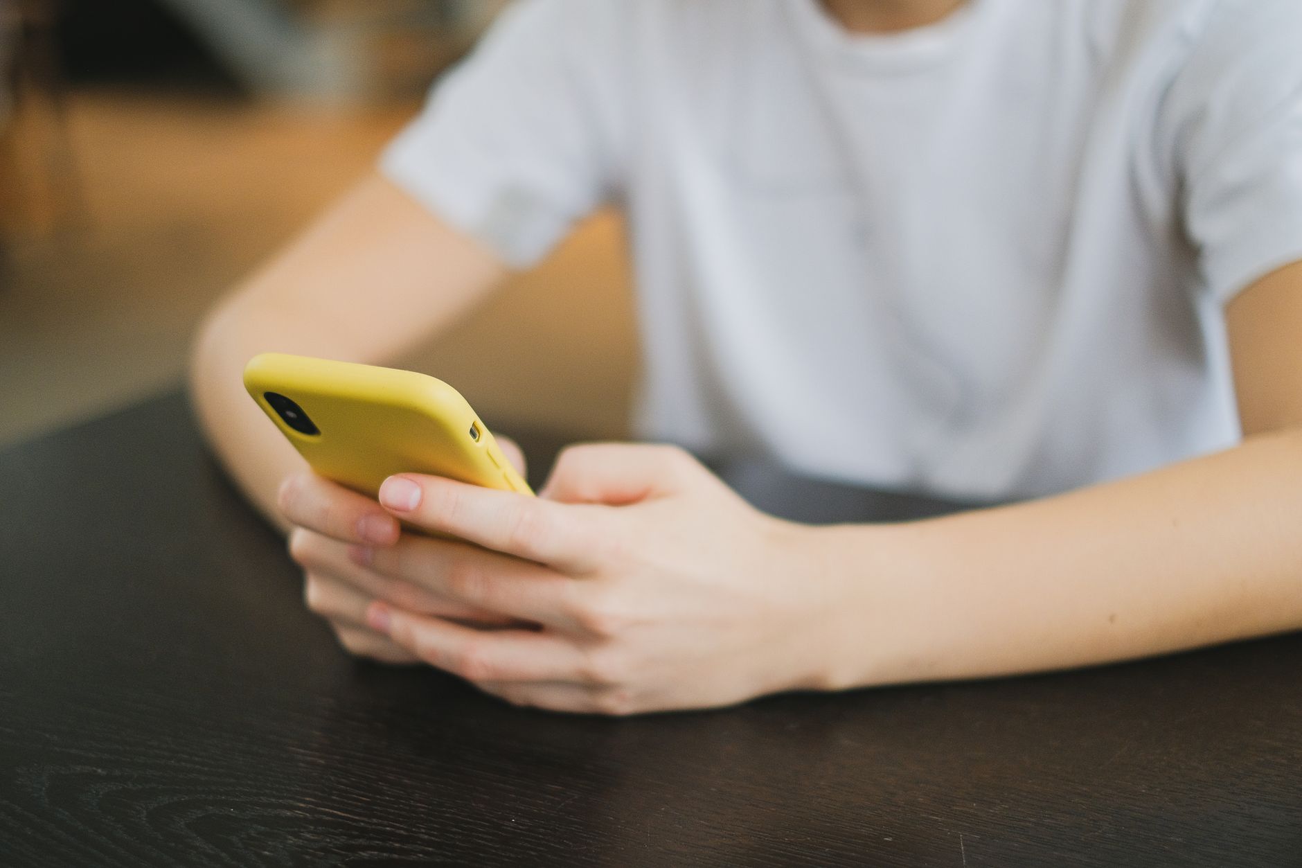 Mains d'une personne en t-shirt blanc tenant un téléphone jaune posé sur une table noire