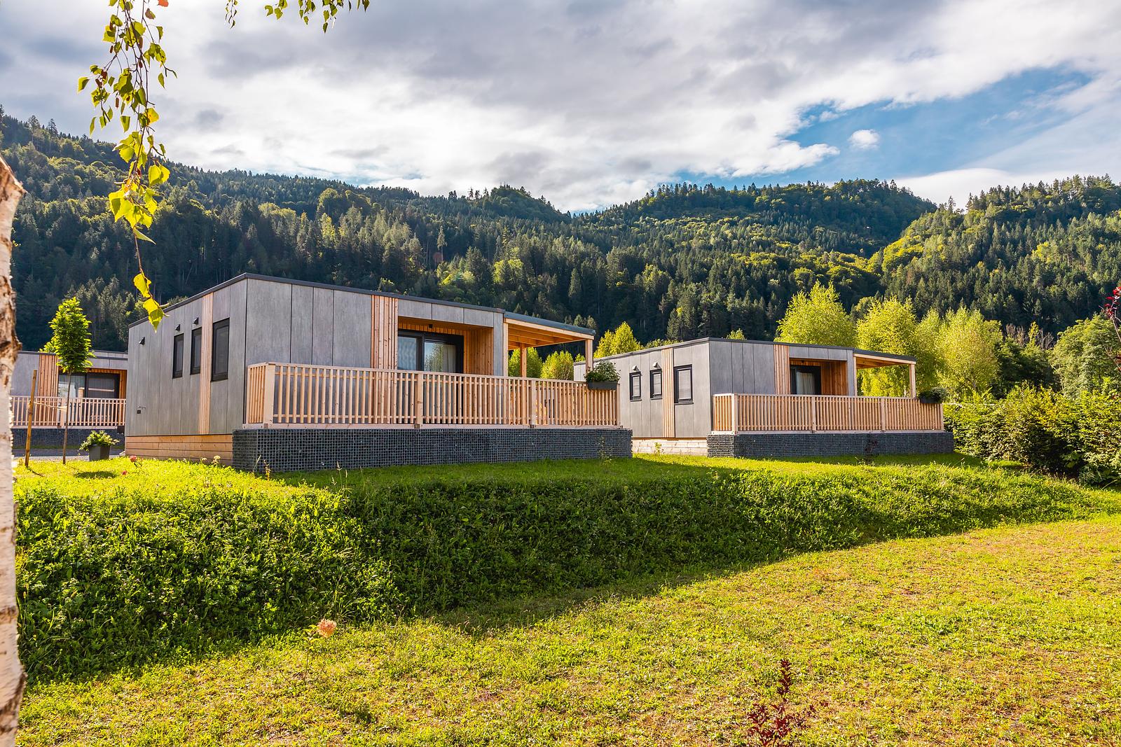 Moderne Ferienbungalows aus Holz und Beton mit Balkonen vor bewaldeten Hügellandschaft