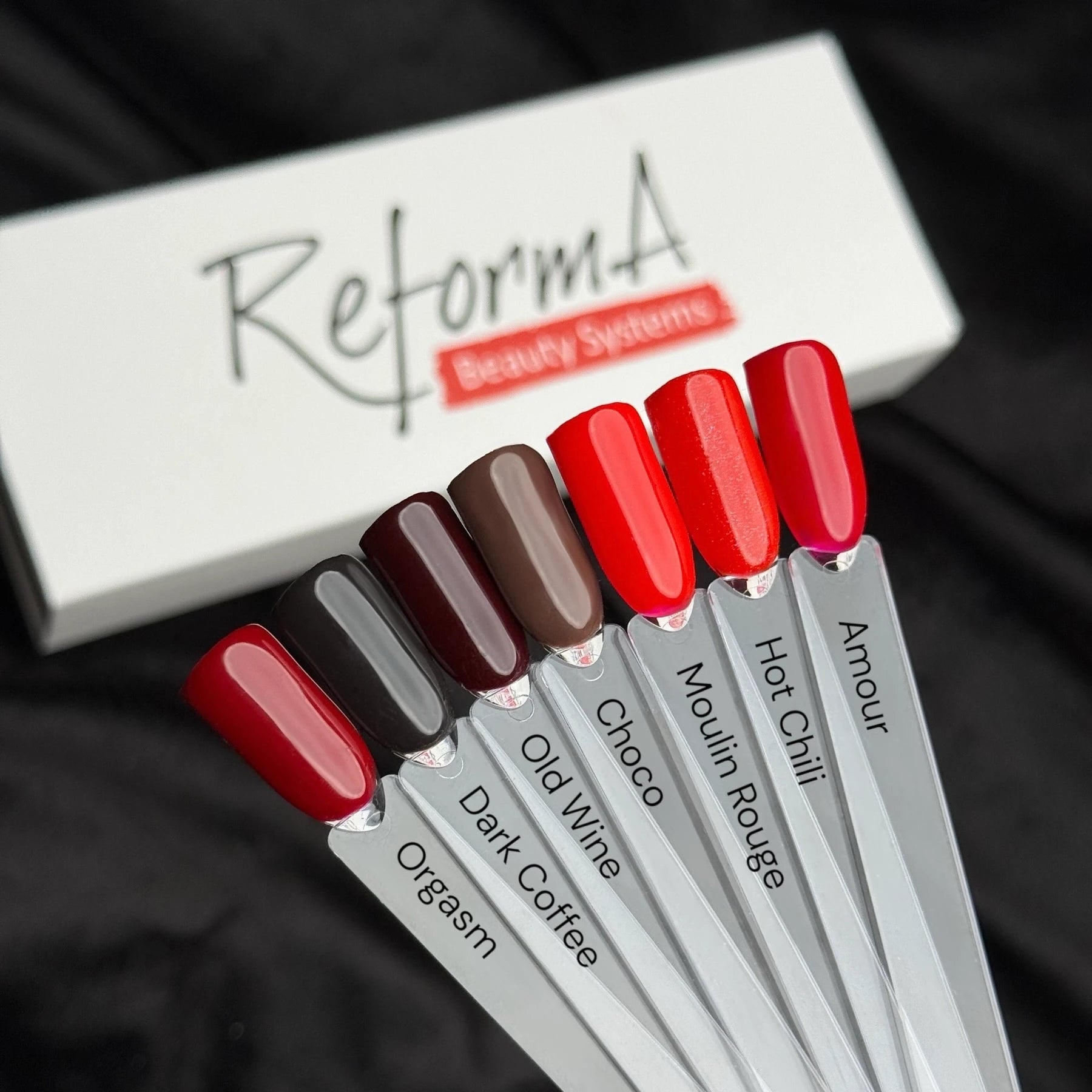 Paletka lakierów hybrydowych w odcieniach od czerwieni do ciemnego brązu z etykietami nazw kolorów i pudełkiem ReformA Beauty Systems