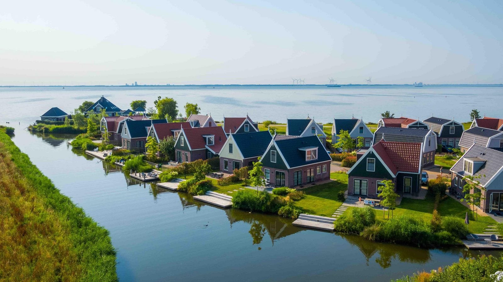 Luftaufnahme von Ferienhäusern mit roten und dunklen Dächern an Wasserkanalreihen in niederländischer Landschaft