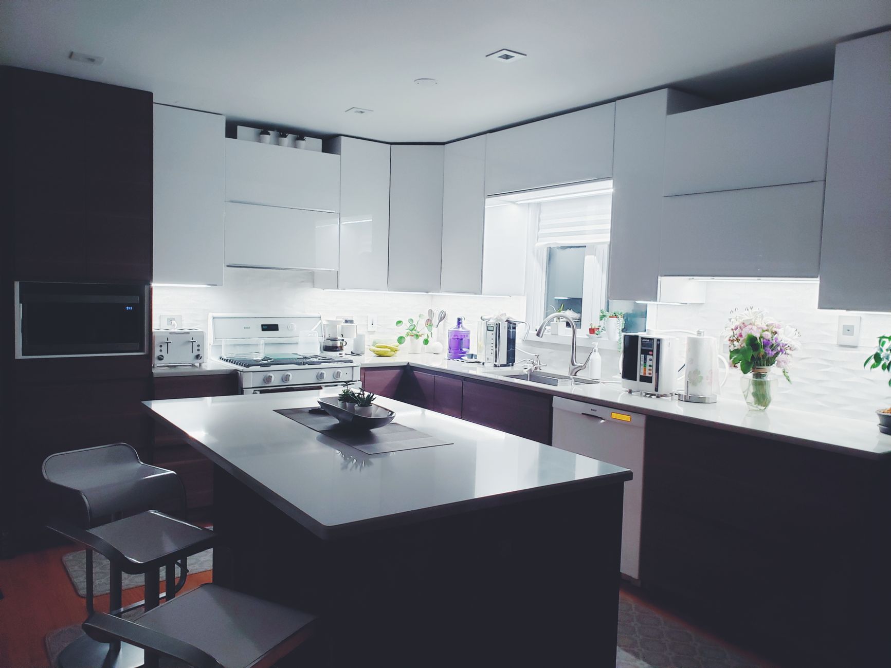 Elegancka kuchnia z białymi szafkami górnymi, czarnym wyspą kuchenną i białym blatem, oświetlona led strip lights