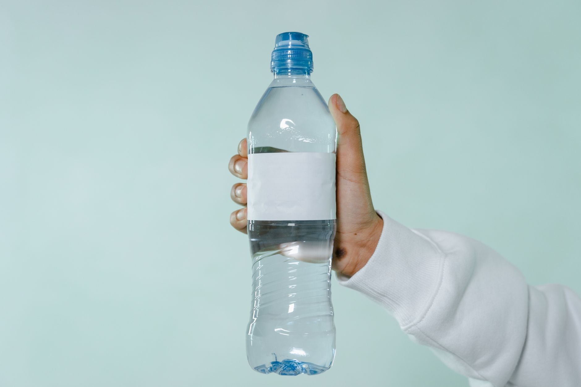 Person holding a plastic water bottle with blank label against light blue background