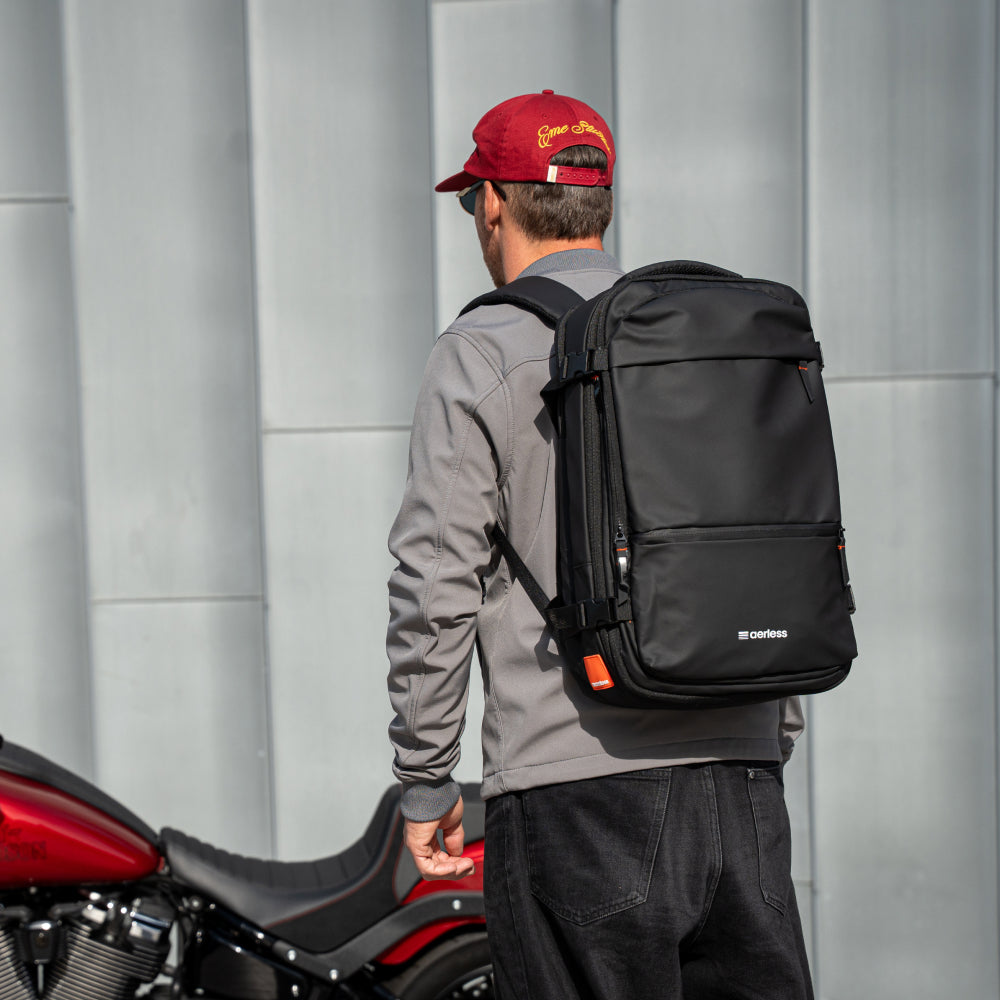 Man wearing red cap and gray jacket carrying black backpack with orange accents on his back